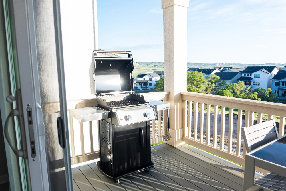 Churrasqueira a gás moderna em aço inox posicionada na varanda de um apartamento com vista para a cidade, pronta para uso.